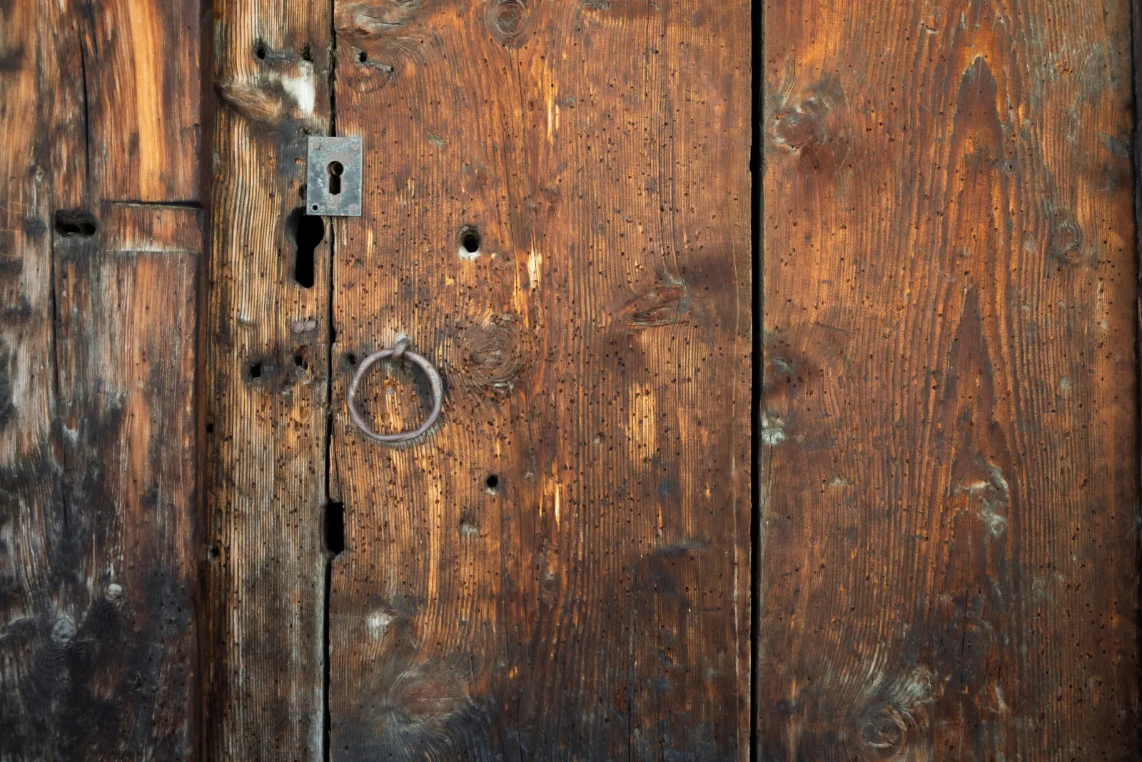 Old worm-eaten wooden chalet door with a metal ring and lock