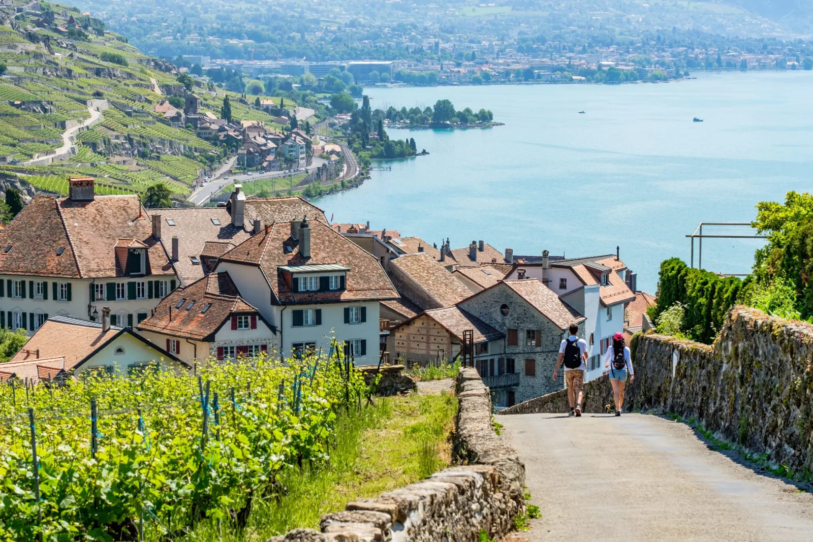 Two walkers on a path between the vines and a Lavaux village, above Lake Geneva