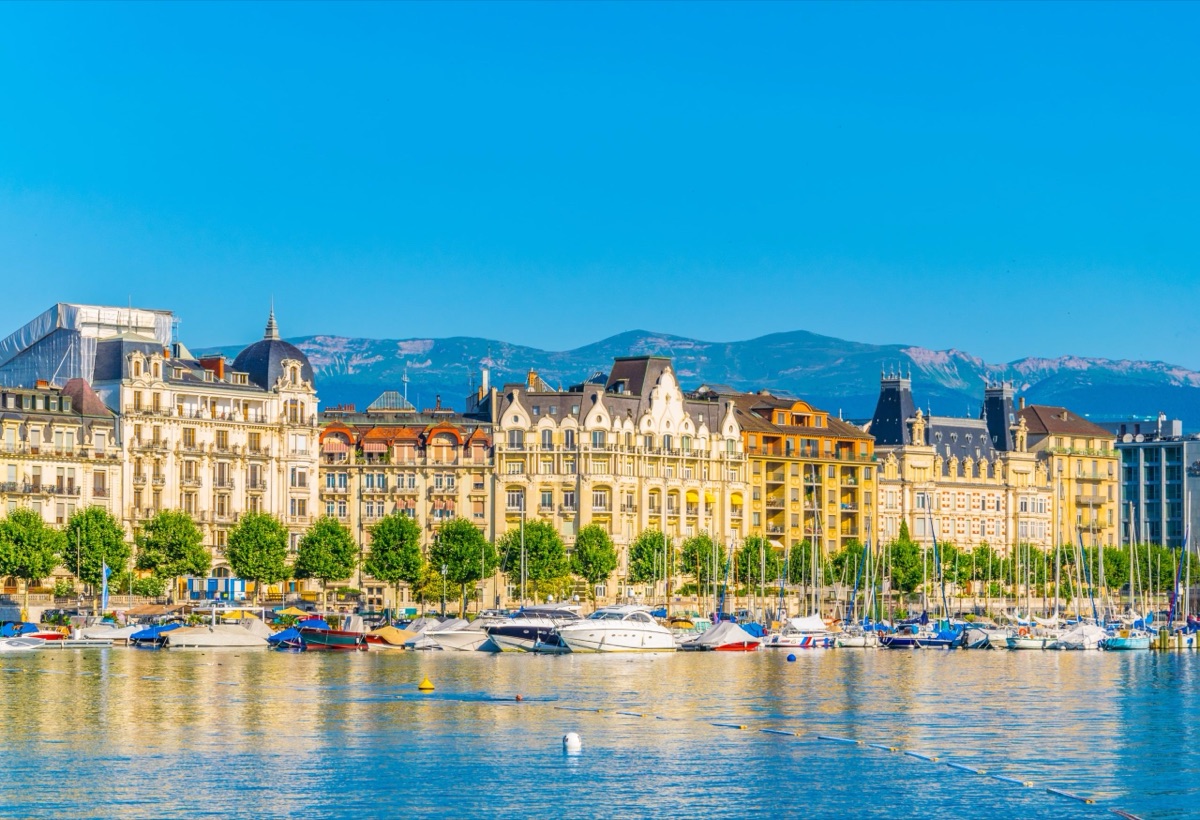 Old buildings and moored boats on the right bank of Lake Geneva in Geneva, mountains in the background