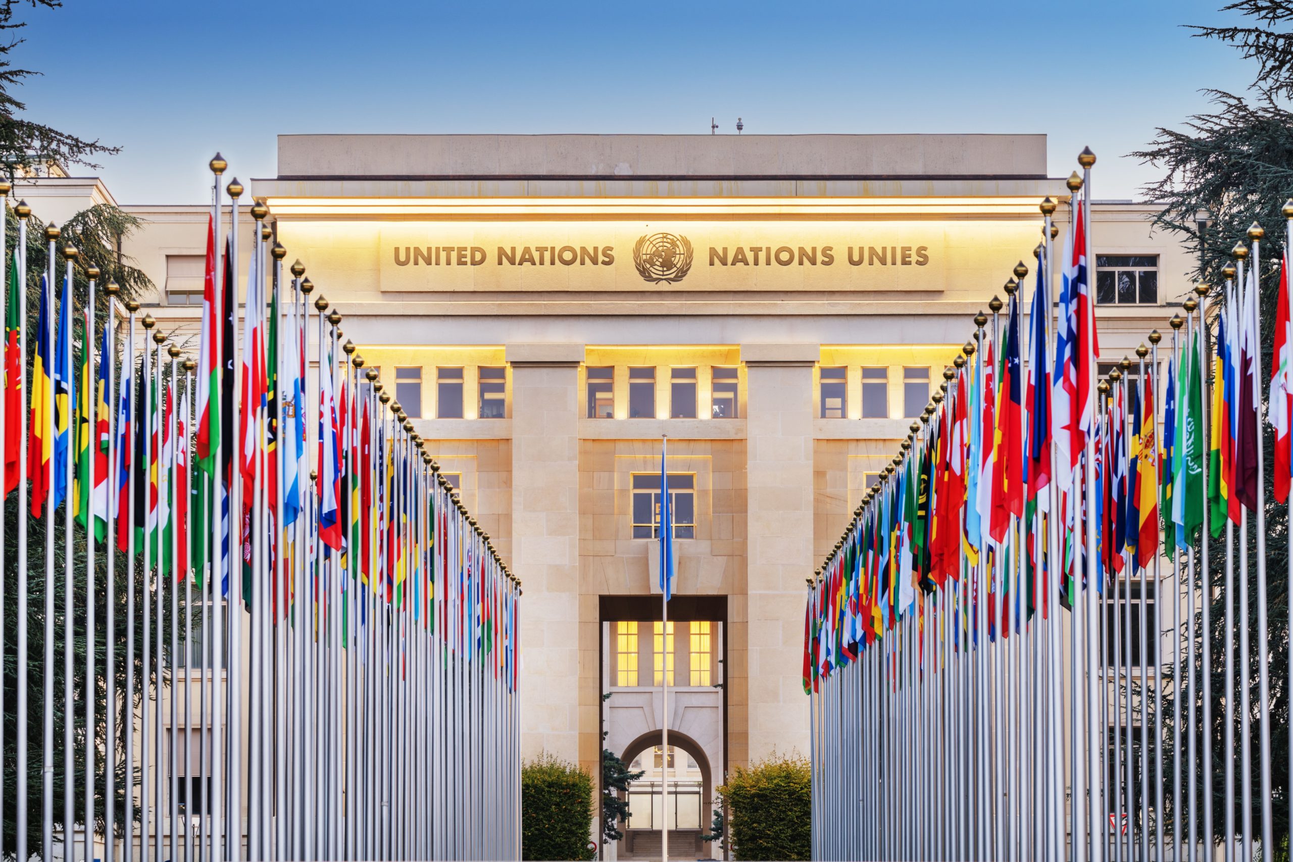 Façade du Palais des Nations à Genève avec les drapeaux des pays membres de l’ONU alignés.