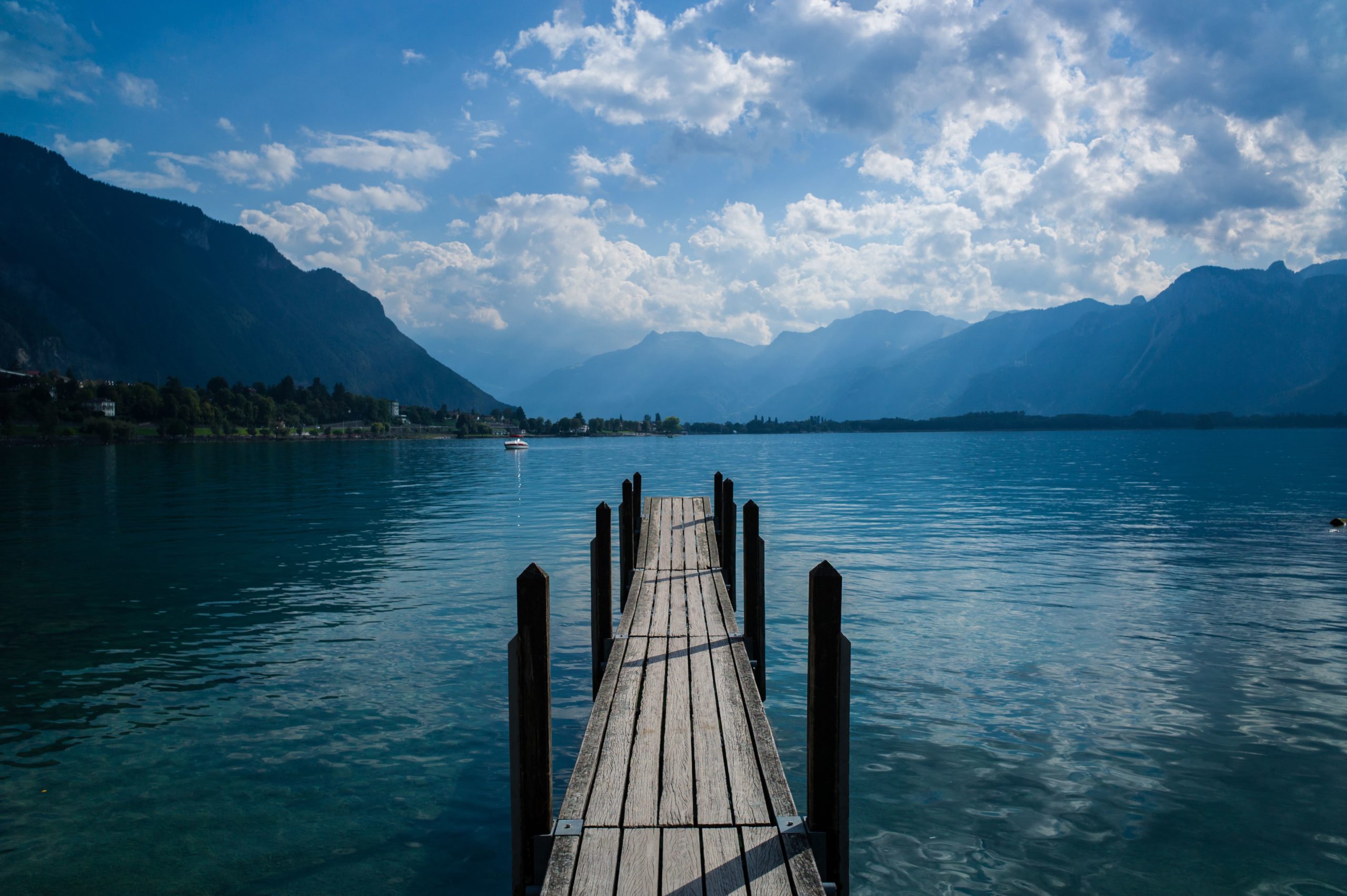 Ponton en bois avançant sur le lac Léman avec vue dégagée sur les montagnes et le ciel nuageux.
