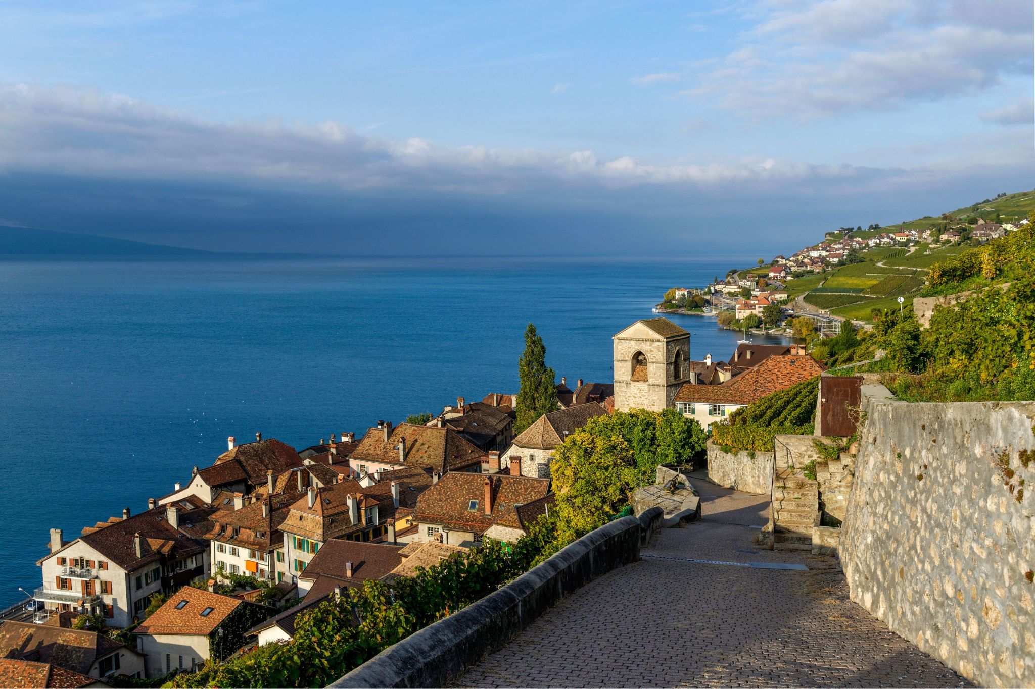 Vue des vignobles en terrasses de Lavaux avec village au bord du lac Léman et collines environnantes.