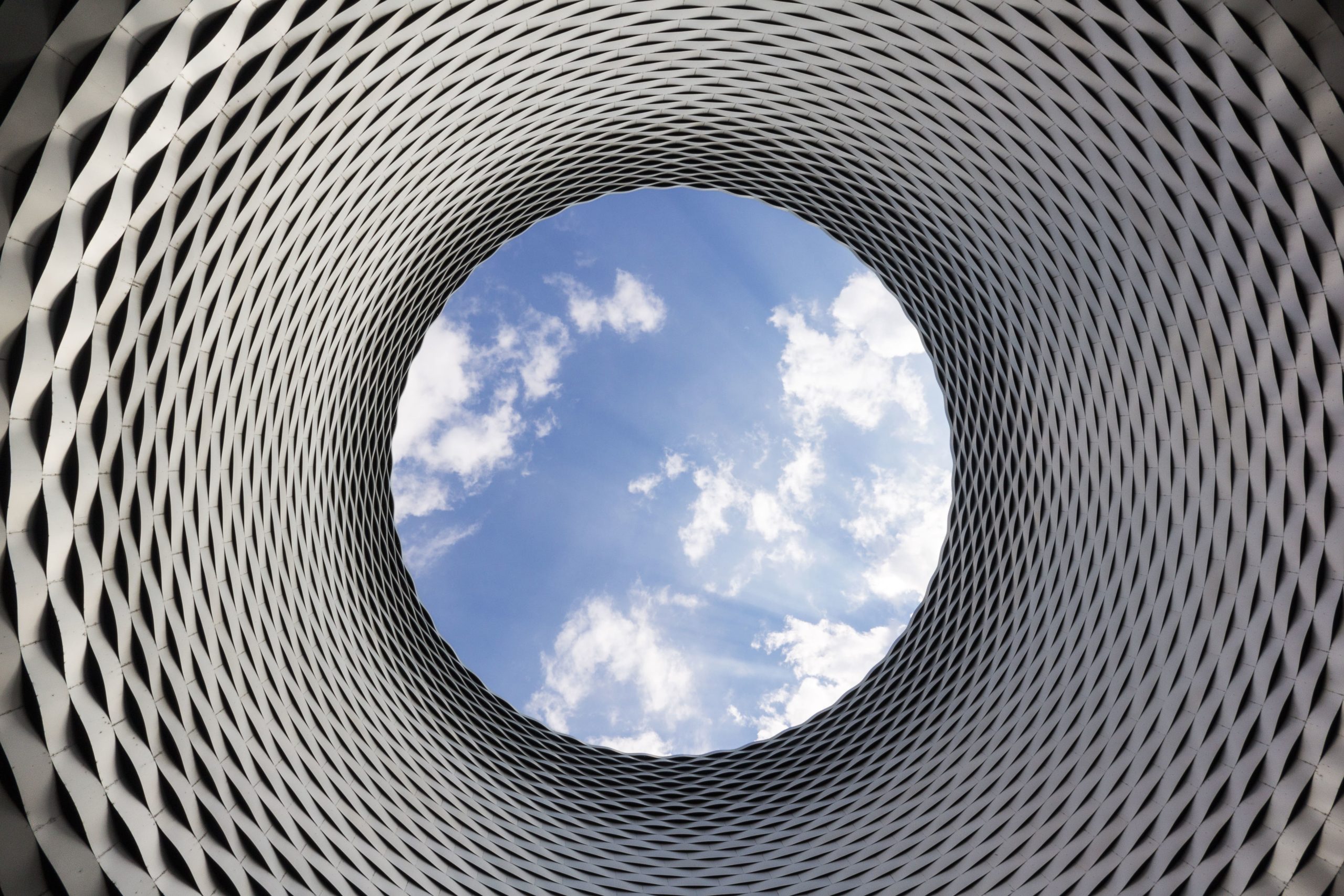 Vue architecturale du toit circulaire du centre d’exposition de Bâle, conçu par Herzog & de Meuron, laissant apparaître le ciel bleu et des nuages à travers l’ouverture centrale.